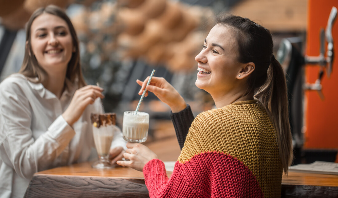 Two happy women are sitting in a cafe, drinking milkshakes,